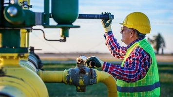 Engineer in yellow hard hat turning a valve on a yellow gas pipeline