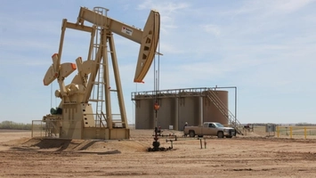 Oil pumpjack with cylindrical storage tanks and a pickup truck at a production site