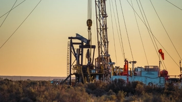 Oil drilling rig and pump jack at sunset with scrubland in the foreground