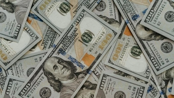 Close-up of overlapping US $100 bills showing Benjamin Franklin portraits and blue security strip details