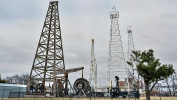 Wooden oil derrick and steel drilling towers at an outdoor oil and gas heritage site under an overcast sky