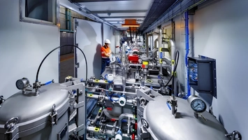 Worker in orange safety gear operating valves and instrumentation inside a modular EOR processing skid