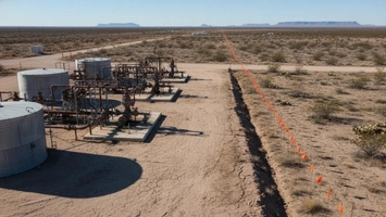 Oil production equipment with rusted pipe fittings and storage tanks across dry cracked desert terrain