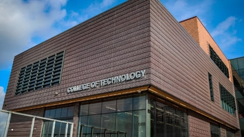 College of Technology brick building exterior with large glazed ground-floor windows under a partly cloudy sky